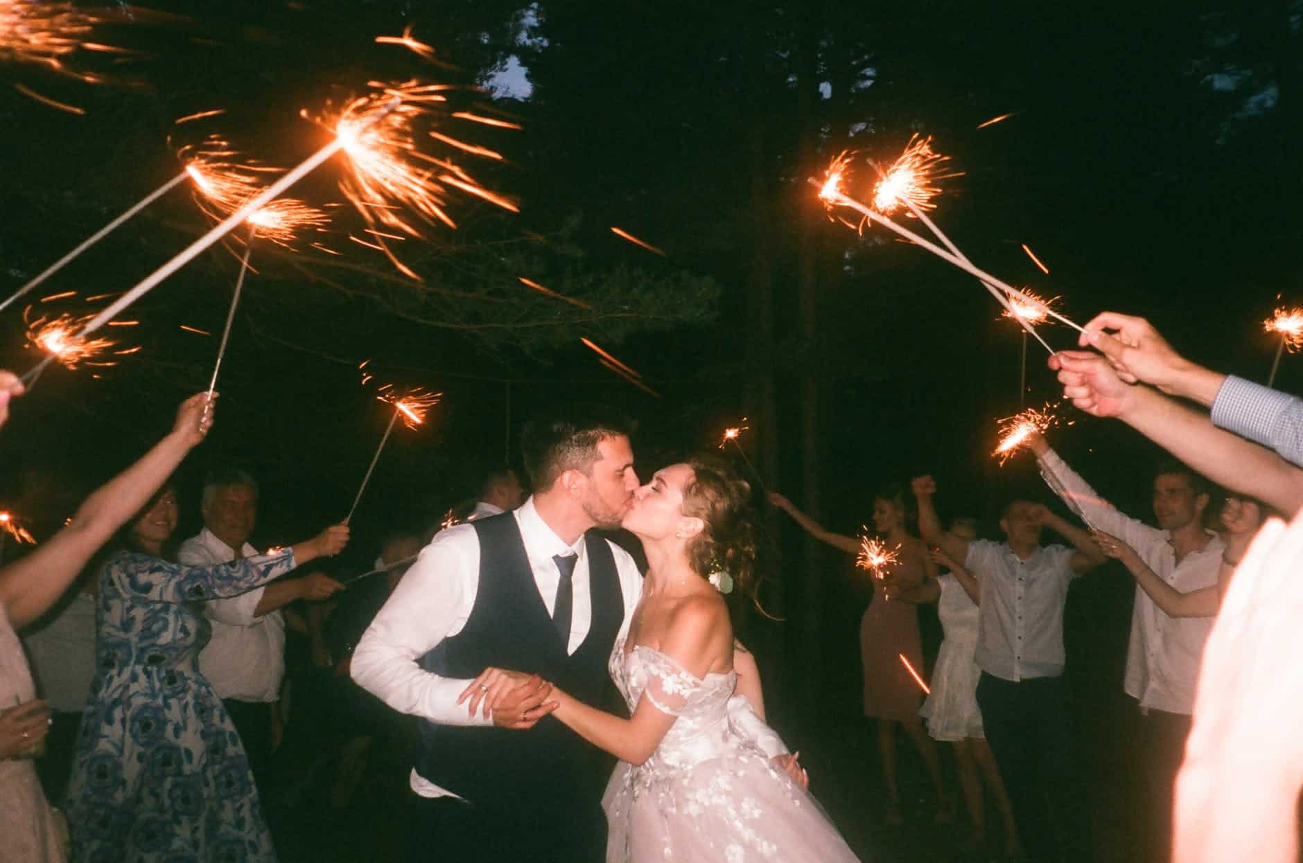 people raising lit sparklers while encircling bride and groom kissing