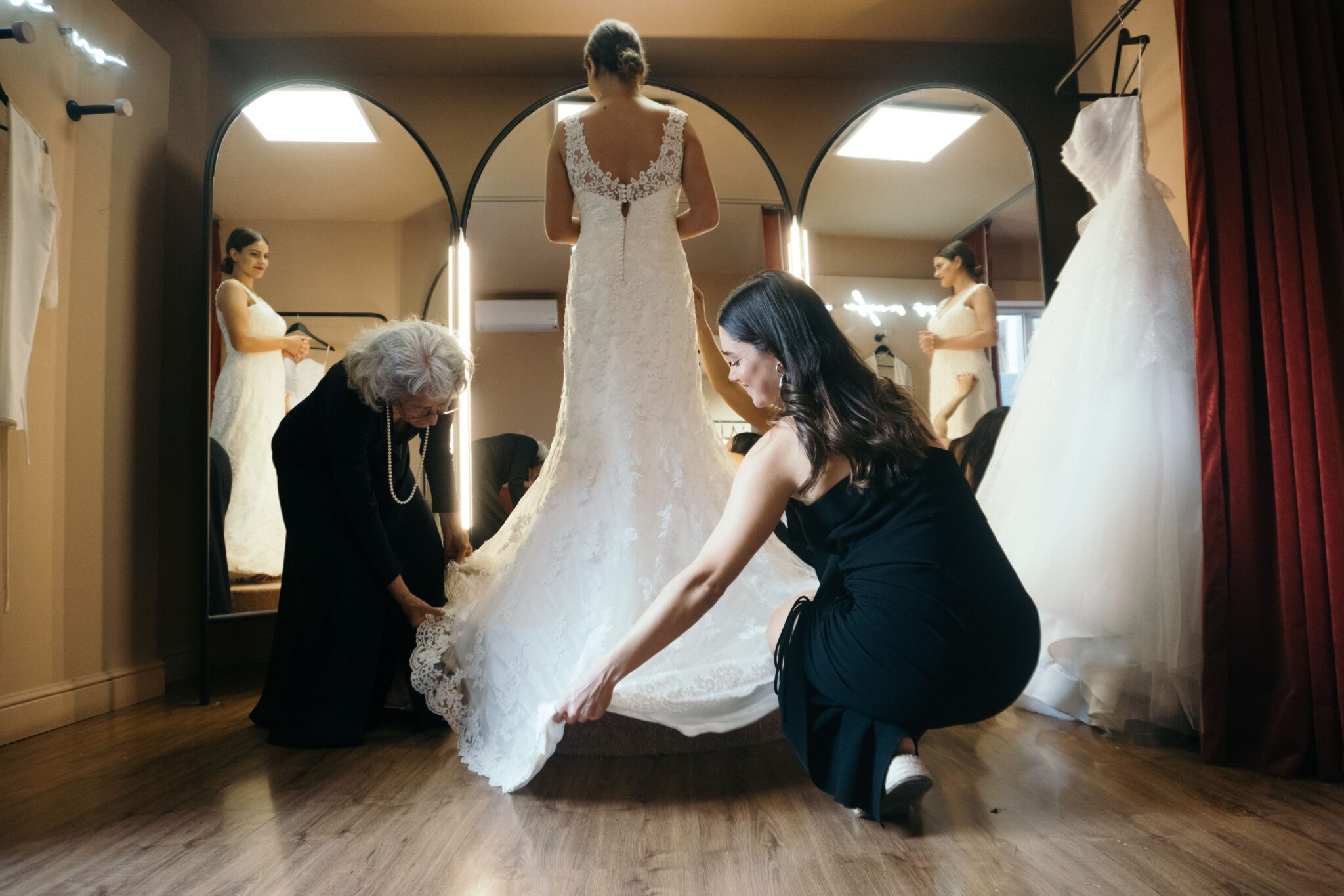 Essayage de robe de mariée dans une boutique avec les vendeuses qui ajustent la robe et la traine pour que la mariée puisse se découvrir