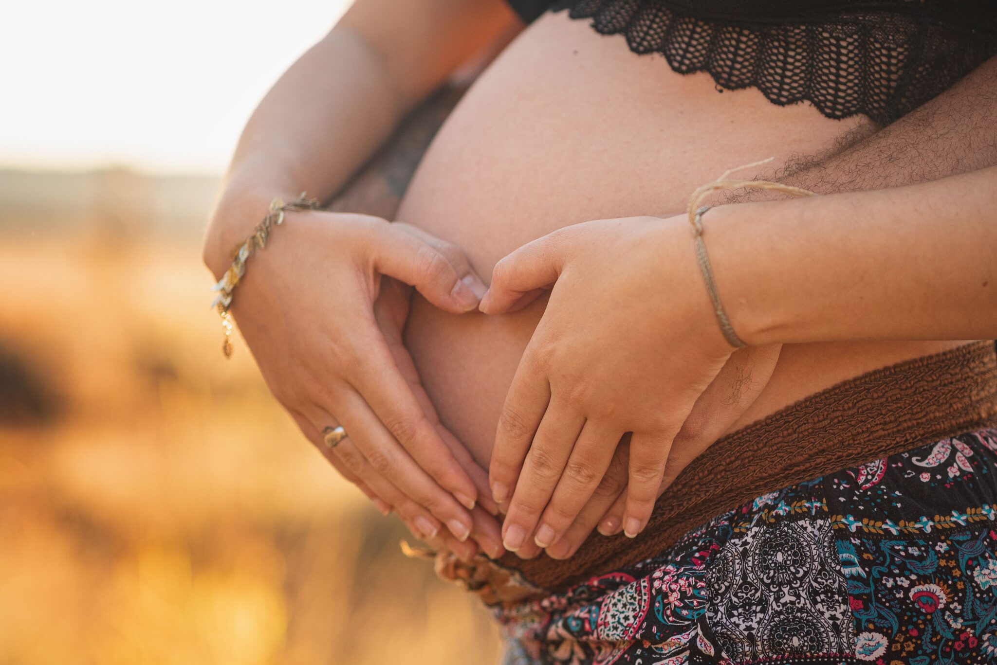 Ventre de femme enceinte pendant sa grossesse avec les mains des futurs parents qui forment un coeur sur le ventre