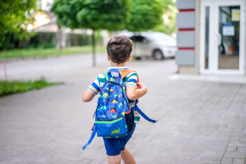 enfant qui va faire sa première rentrée en maternelle avec son sac à dos sur le dos et qui se dirige vers sa nouvelle école