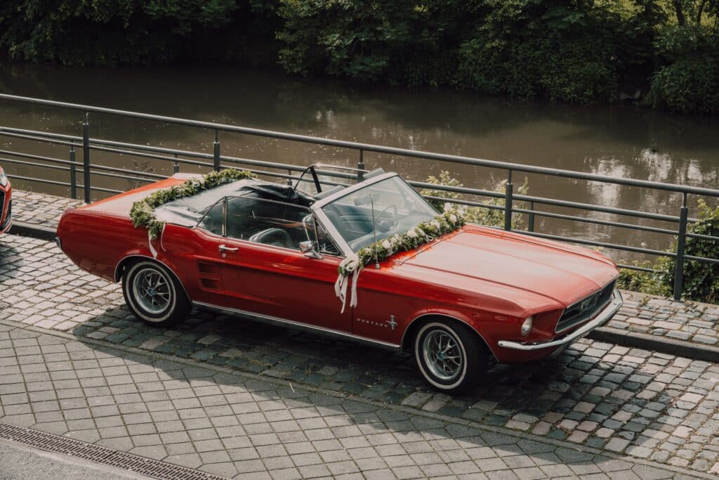 location de voiture de mariage avec une cabriolet rouge décorée avec une guirlande de fleurs et de feuillage
