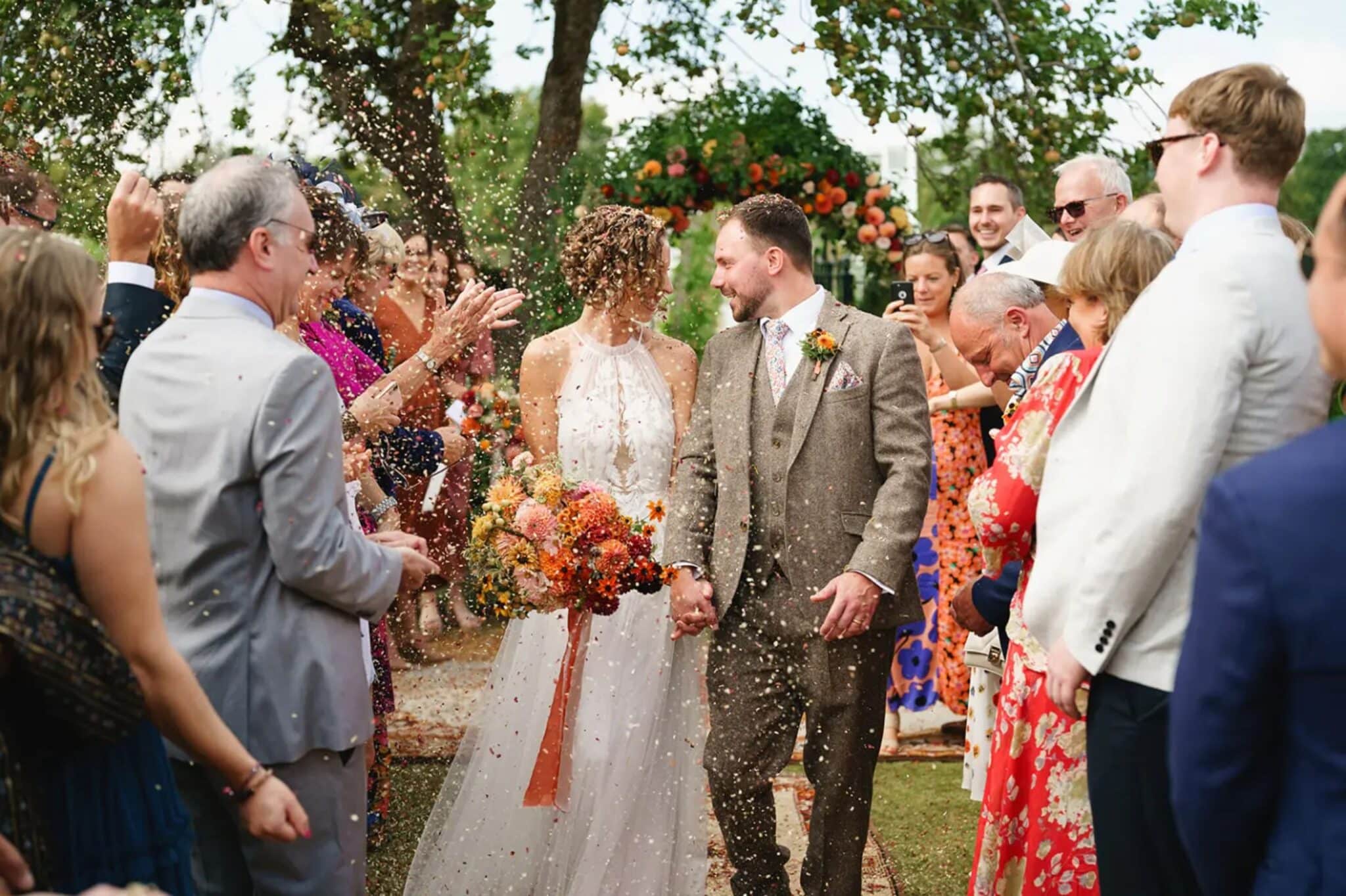photo d'un couple qui sort de sa cérémonie laïque sous une pluie de pétales et entourés de leurs invités