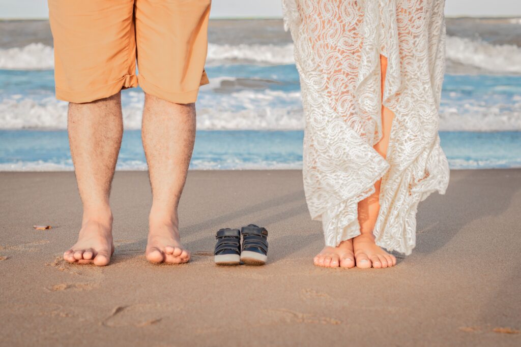 annonce de grossesse sur la plage avec les pieds des futurs parents et une paire de chaussures pour bébé